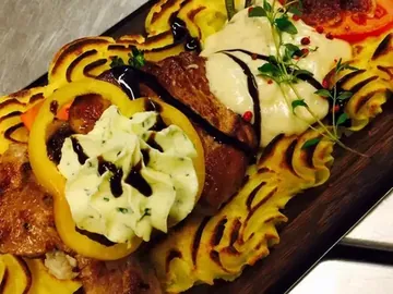 Viande sur planche de bois avec purée, poivron et herbes fraîches